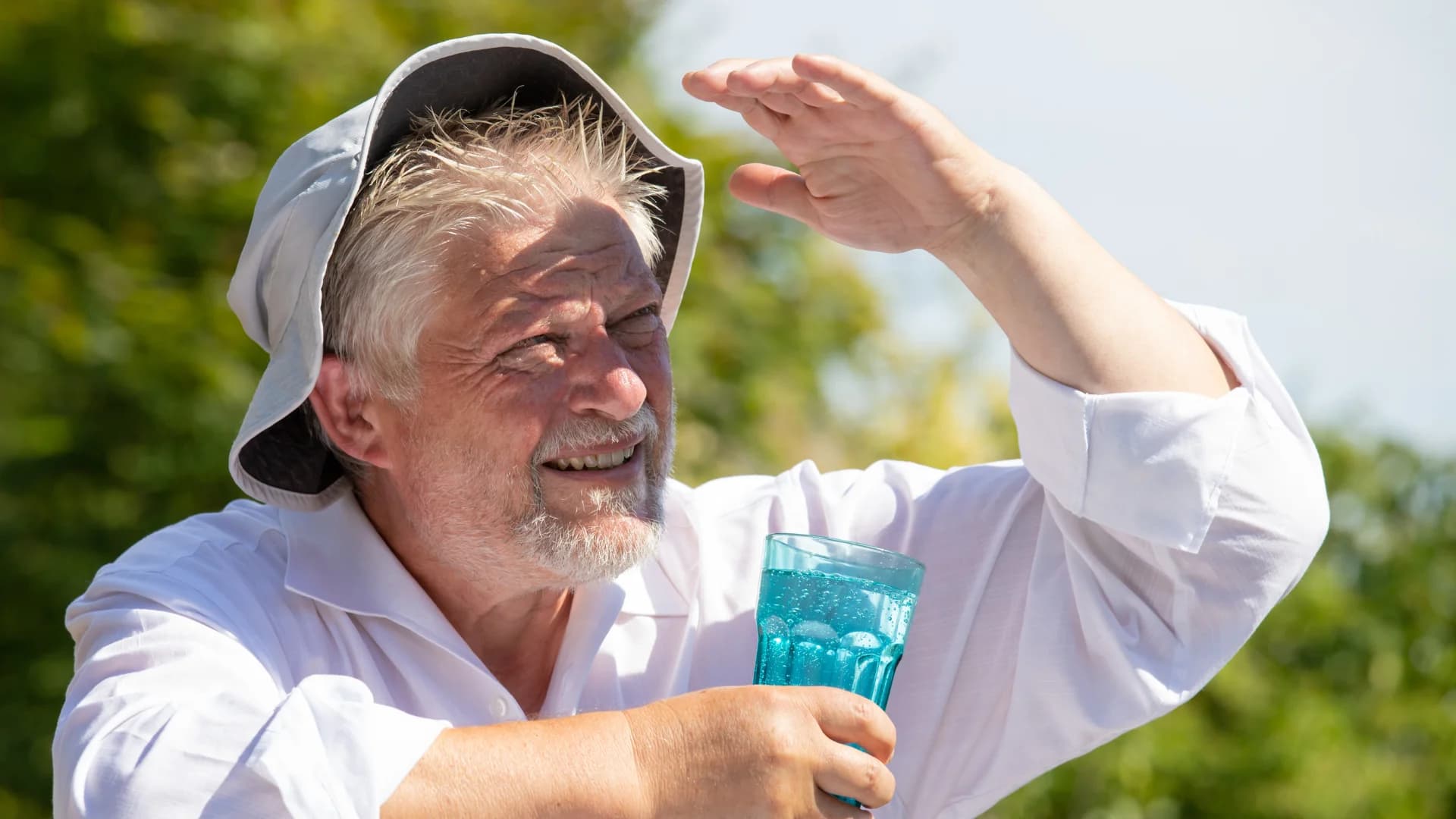 Older man holding a glass of water and shading his face from the sun